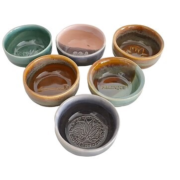 Custom stamped ceramic copitas de mezcal arranged in a set, showing handmade stoneware glaze variation and interior stamp detail u2014 overhead flat lay on a dark surface